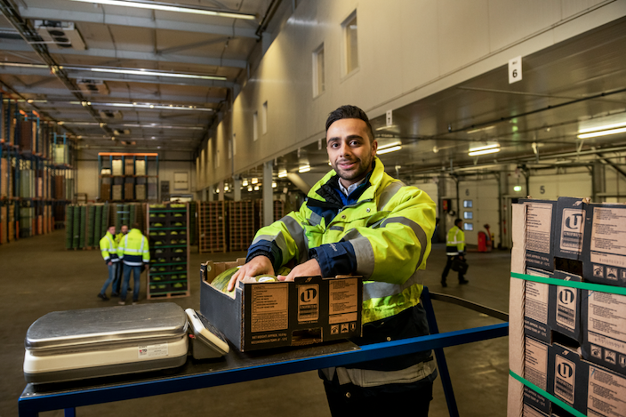 A warehouse specialist in a high-visibility jacket handling fresh produce boxes in a modern cool store